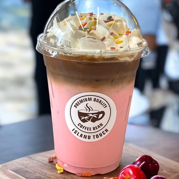 Pink and brown layered iced coffee with whipped cream and sprinkles, next to cherries and nuts.