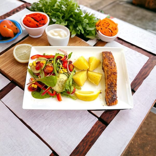 Grilled salmon fillet with roasted potatoes, fresh salad, and lemon wedges on a white plate.